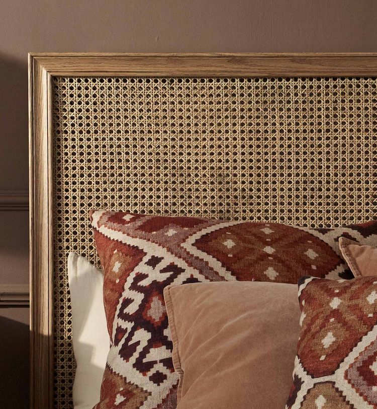 A woven wicker headboard with brown and patterned pillows on the rattan bed.