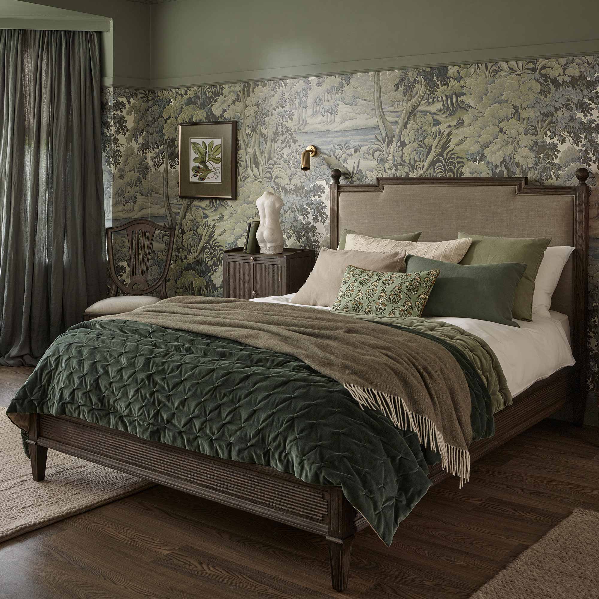 Elegant bedroom with a forest-themed wallpaper, wooden bed, green and brown bedding, and a decorative chair. Warm lighting and earthy tones.