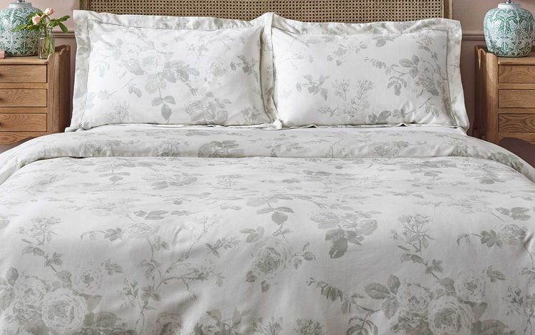 A neatly made bed with floral-patterned bedding, wooden headboard, and matching nightstands with lamps and decorative vases.