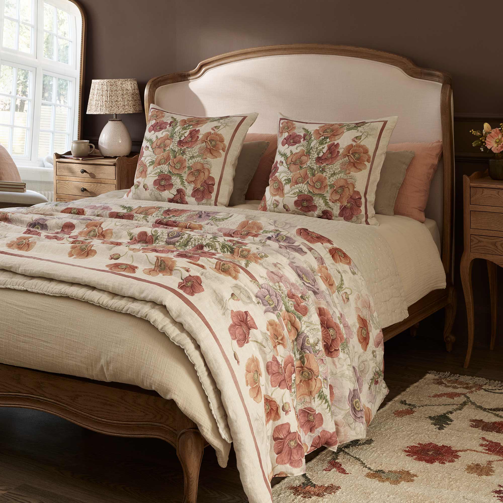 Cozy bedroom with a wooden bed, floral bedding, matching pillows, and a bedside table with a lamp. Warm lighting and a floral rug enhance the decor.