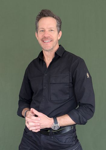 Smiling man in a black shirt stands against a plain green background.