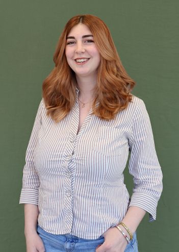 Smiling woman with long hair in a striped shirt and jeans poses in front of a green background.