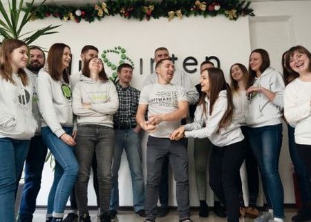 A group of people smiling and laughing in front of a wall with a logo, decorated with garland.