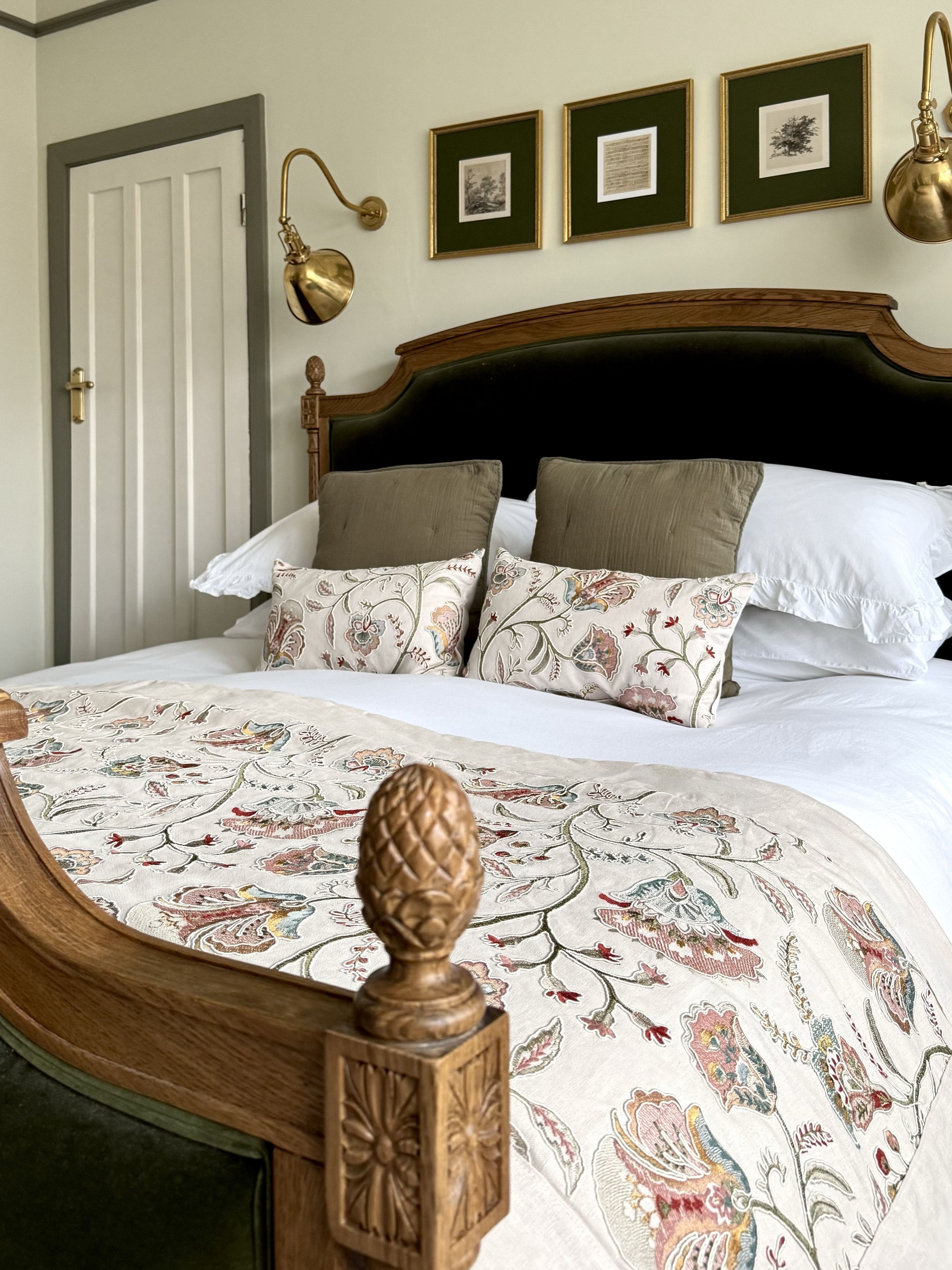 Green velvet bed with ornate carved details and floral embroidered bedding.