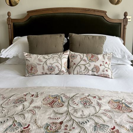 Dark Green velvet upholstered bed with acorn finials covered in a beige and pink floral bedspread