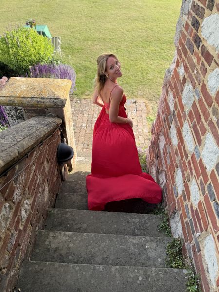 Woman in a red dress stands on stone steps, smiling back, on the grounds at Glyndebourne.