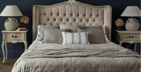 Elegant bedroom with a tufted headboard, beige bedding, and matching nightstands with lamps and decorative vases against a dark wall.