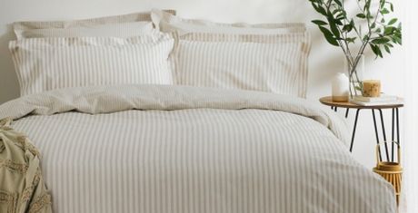 A neatly made bed with striped bedding, next to a small round table holding a plant, candle, and decorative items.
