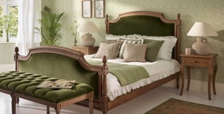 Elegant bedroom with a vintage-style bed featuring green upholstery, matching bench, wooden nightstands, and soft lighting. Green patterned wallpaper.
