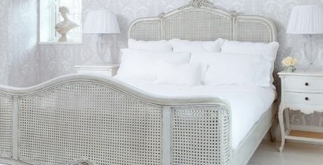 Elegant bedroom with a vintage white wicker bed, white bedding, matching nightstands, and soft lighting from table lamps.