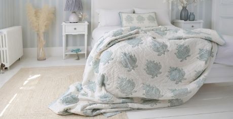 Cozy bedroom with a bed covered in a quilt with blue floral patterns, white furniture, and soft lighting. Neutral and calming decor.