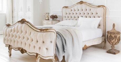 Elegant bedroom with a vintage-style bed featuring tufted headboard and footboard, white bedding, and ornate decor in a bright, airy room.