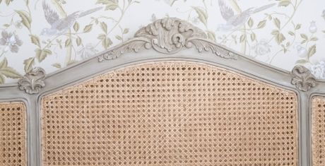 A vintage-style headboard with intricate wickerwork and ornate wood detailing, set against floral wallpaper with bird motifs.