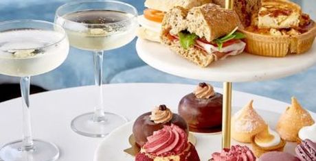 A tiered stand with sandwiches, pastries, and desserts, accompanied by two glasses of champagne on a white table.