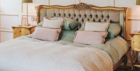 Elegant bedroom with a tufted headboard, green bedding, and pink pillows. Wooden nightstands with lamps flank the bed.