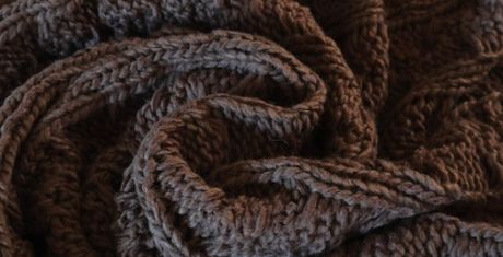 Close-up of a textured, dark brown knitted fabric with intricate patterns and folds.