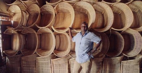 Man standing in front of a wall stacked with large woven baskets, smiling and posing with one hand on his hip.