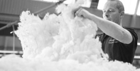 Man working with large pile of fluffy white material in an industrial setting, focused on his task. Black and white image.