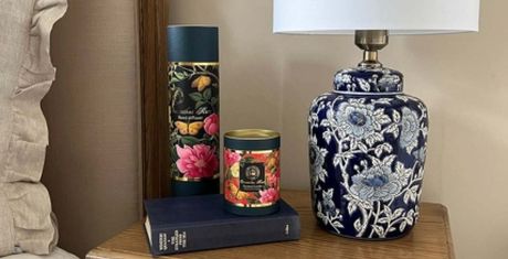 A floral-patterned lamp on a wooden table with a book and two decorative floral tins beside it.