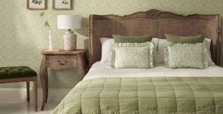 Cozy bedroom with a wooden headboard, green bedding, patterned pillows, a bedside table with a lamp, and botanical wall art.