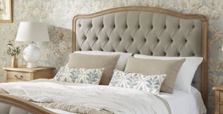 Elegant bedroom with a tufted headboard, patterned wallpaper, and a neatly made bed with decorative pillows and a white lamp on a wooden nightstand.