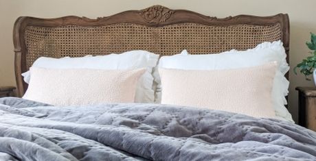 A cozy bed with a carved wooden headboard, white pillows, and a plush gray quilt, set against a neutral wall.