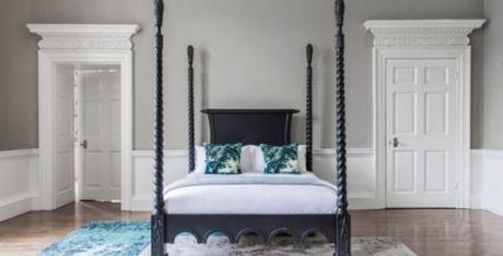 Elegant bedroom with a black four-poster bed, white bedding, decorative pillows, and ornate moldings on doors and walls.