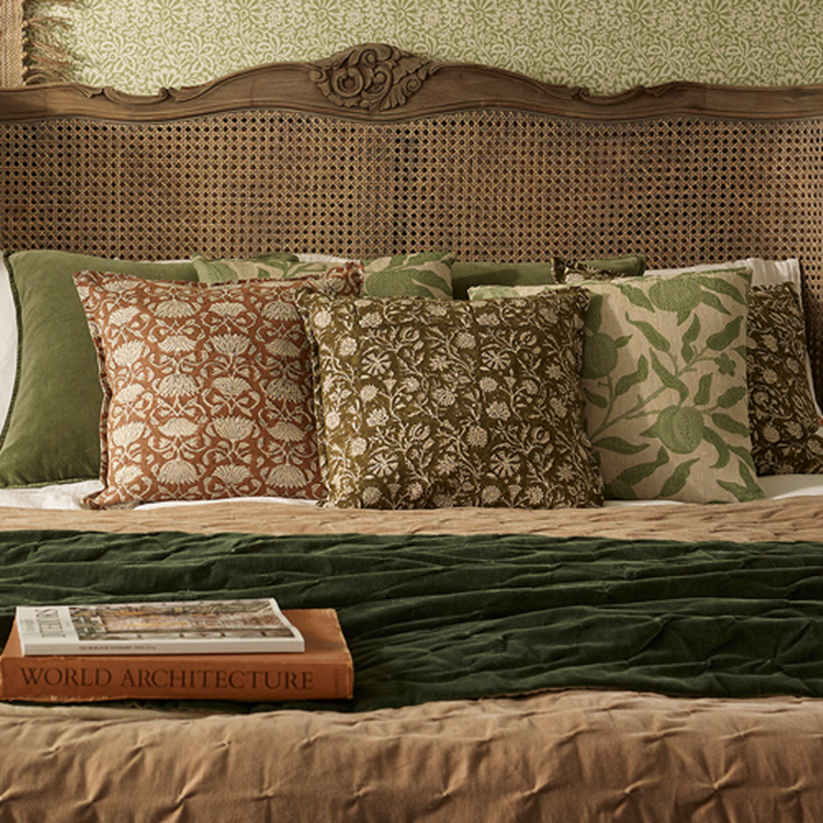 A cozy bed with patterned green and brown pillows, a textured green blanket, and a book titled "World Architecture" on the edge.