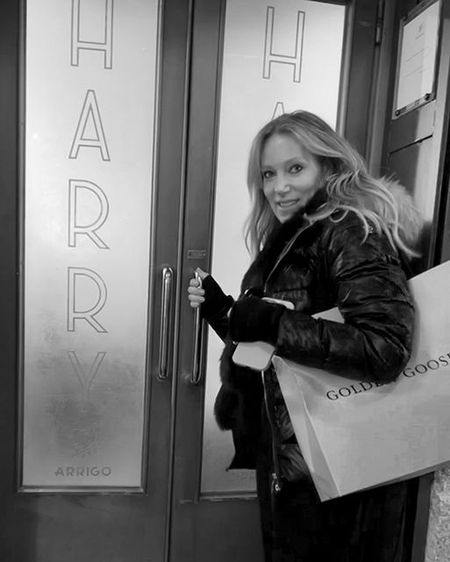 Woman in a coat holding a shopping bag, standing at a door with "HARRY" written on glass panels.
