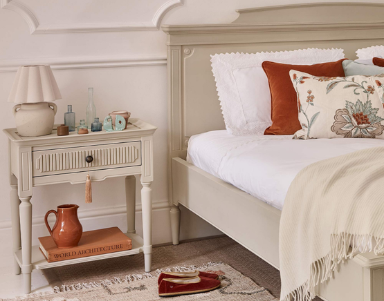 Neutral bedroom with a beige nightstand and a bed with floral pillows and a draped blanket.