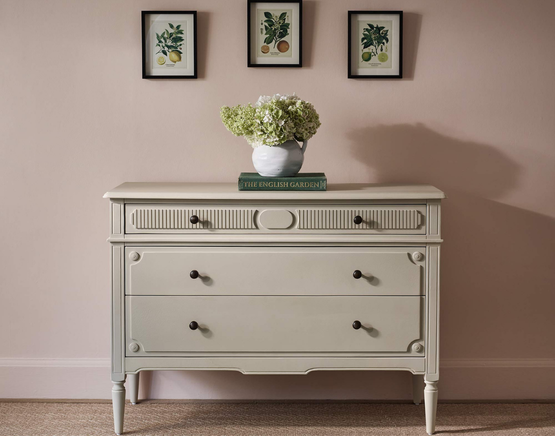 A cream dresser with decorative handles, set against a wall with three citrus prints.