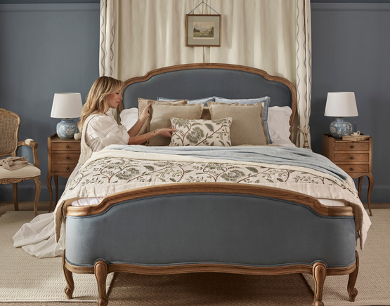 A woman relaxes on a large, velvet bed in a cosy, tastefully decorated bedroom with blue walls and blue and white décor.