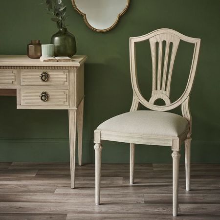 Elegant wooden chair with a cushioned seat next to a vintage desk, set against a dark green wall with a decorative mirror.