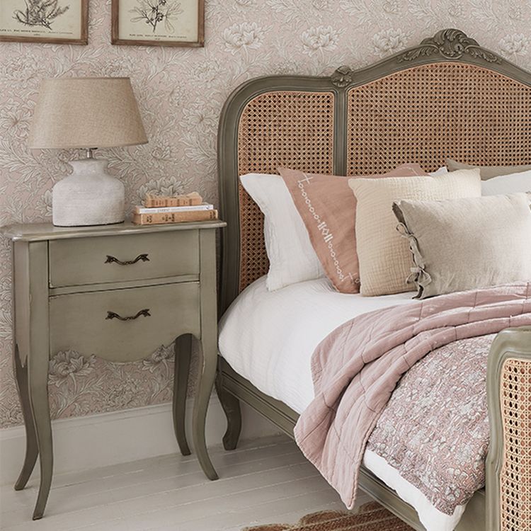 Vintage-style bedroom with a cane headboard, floral wallpaper, a green nightstand, and a bed with pink and beige bedding.