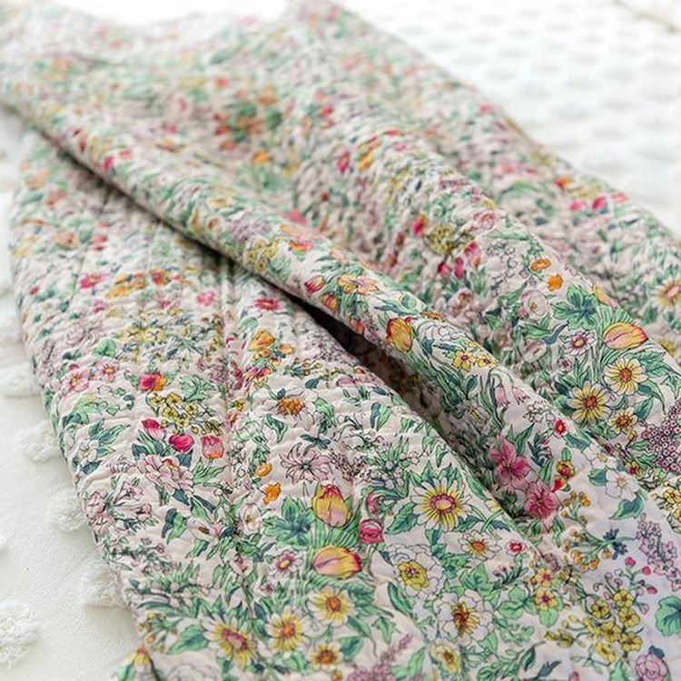 A colorful floral quilt with intricate patterns lies on a textured white surface, featuring various flowers and leaves in vibrant hues.