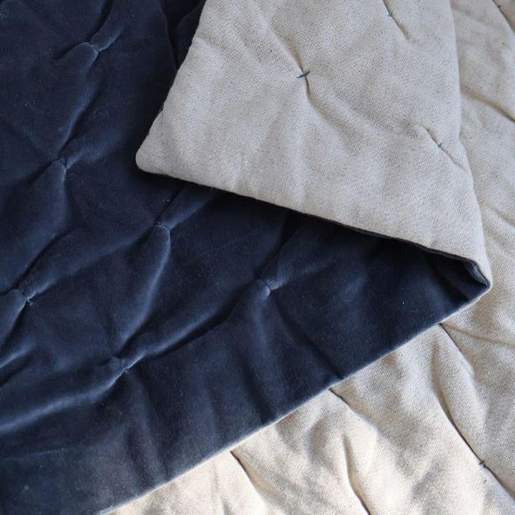 Close-up of a quilt with navy blue and beige fabric, showing quilted stitching and texture.