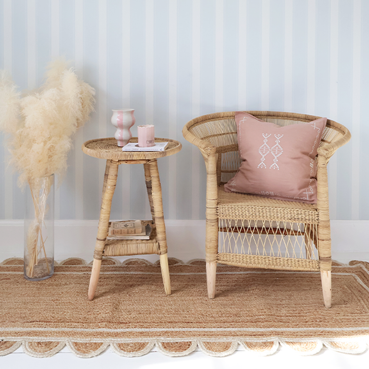 Cozy room with a wicker chair, pink patterned cushion, matching side table, vase with pampas grass, and a striped wall backdrop.