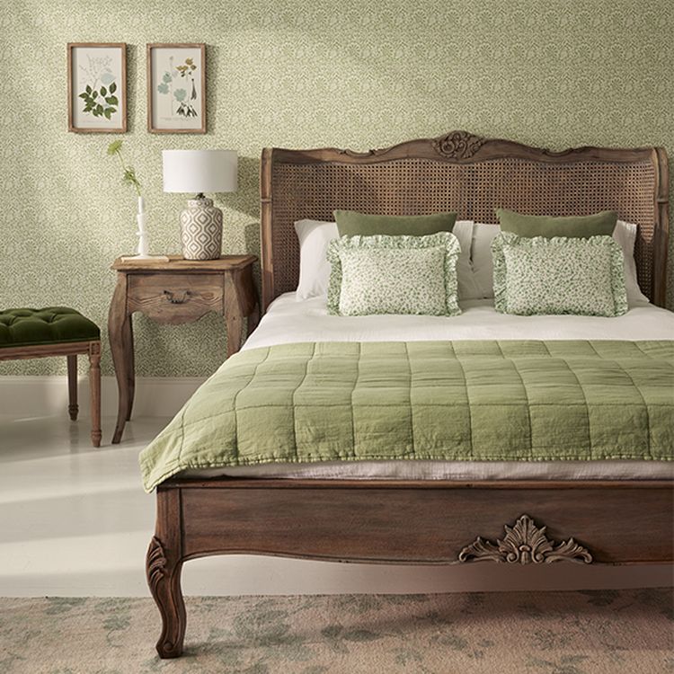 Elegant bedroom with a wooden bed, green bedding, floral-patterned pillows, matching wallpaper, and framed botanical prints on the wall.