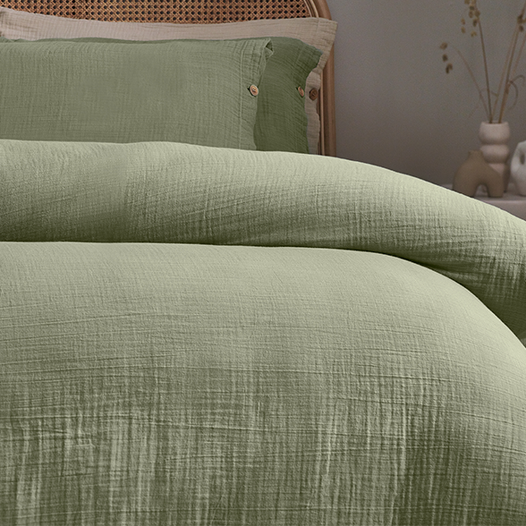 Green textured bedding set on a bed with a woven headboard, featuring a duvet and pillows with button details.