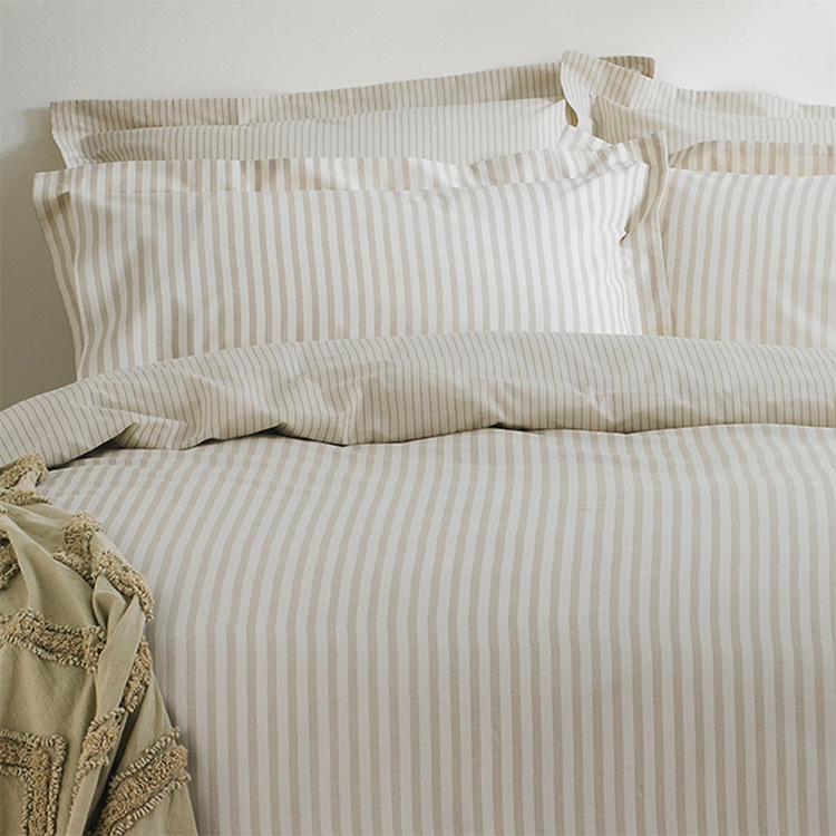 Beige and white striped bedding set with pillows and a textured beige blanket on a bed.