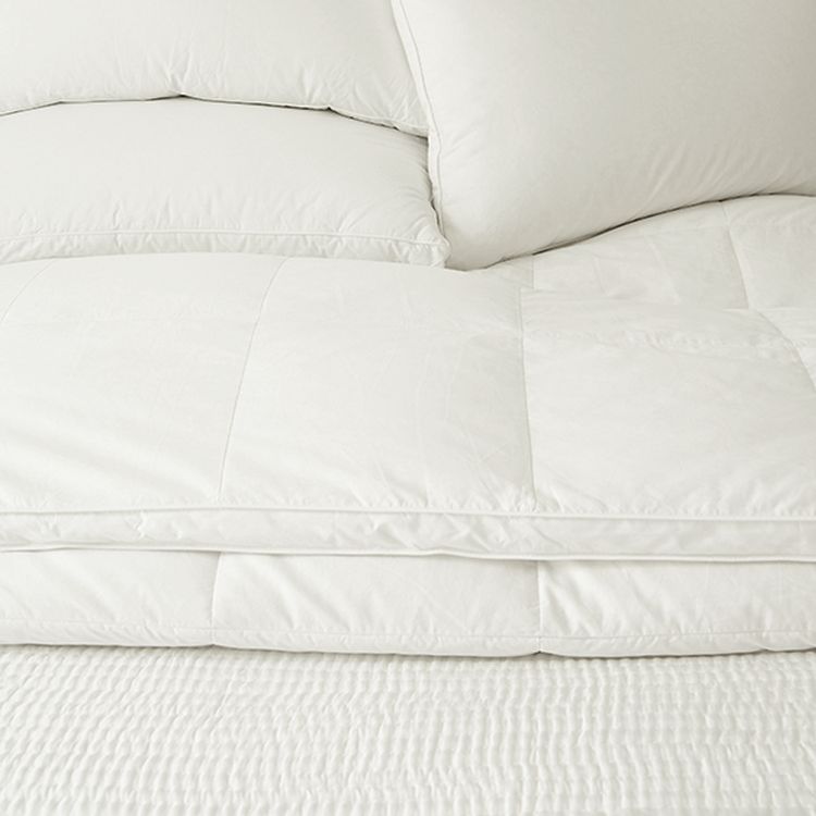 Close-up of a neatly made bed with white pillows and a white quilted comforter, showcasing a soft and clean appearance.