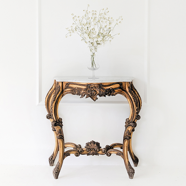 Elegant carved wooden table with a marble top, holding a vase of delicate white flowers, set against a minimalist white background.