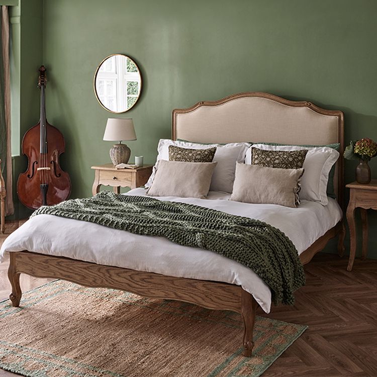 Cozy bedroom with a wooden bed, green walls, a double bass, and a round mirror. Bed has white linens and green throw blanket.