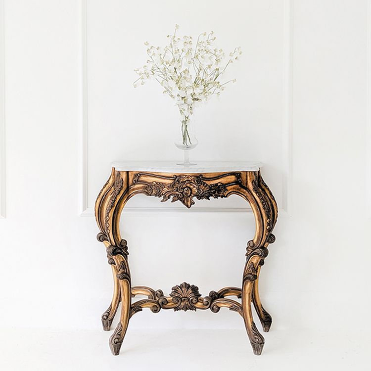 Elegant wooden table with ornate carvings, topped with a white vase holding delicate white flowers, set against a plain white wall.