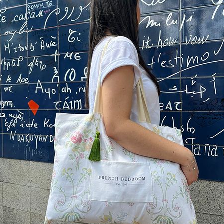 Woman with long hair holding a floral tote bag in front of a blue wall with white script in various languages.