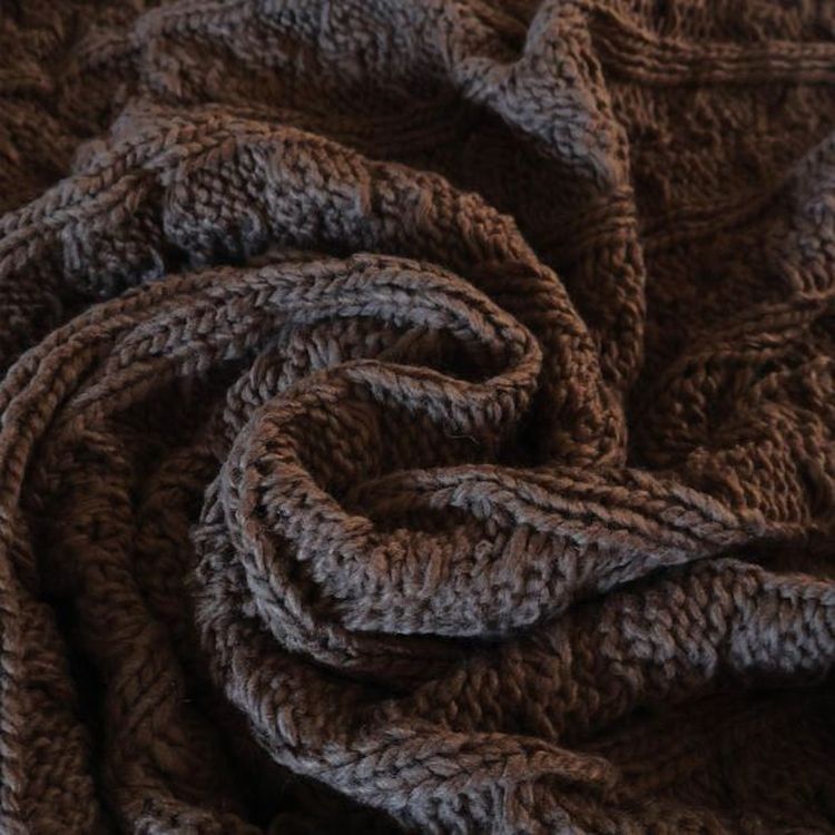 Close-up of a textured, dark brown knitted fabric, intricately woven and arranged in soft, swirling folds.