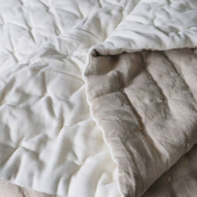 A close-up of a quilt with a white and beige patchwork design, showing textured stitching and soft fabric folds.