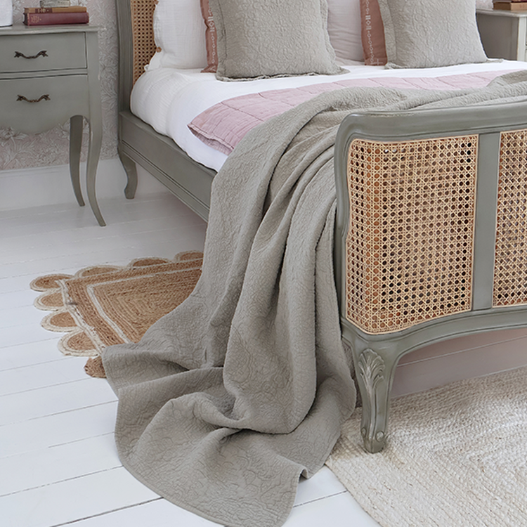 Bedroom with a vintage-style bed, gray quilt, pink pillows, and a bedside table. White walls and floors with a textured rug complete the look.