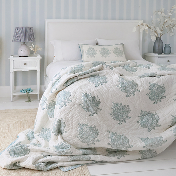 Cozy bedroom with a white bed, floral-patterned quilt, matching pillows, and bedside tables with lamps, set against a striped wallpaper.