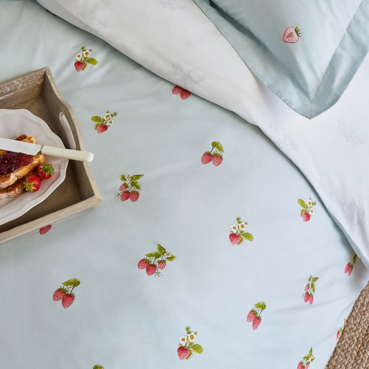 Light blue bedding with small strawberry patterns, accompanied by a wooden tray holding toast with jam and a knife.
